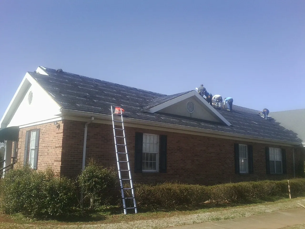 Crew tearing shingles off a brick ranch roof with a ladder set — Emergency Roof Repair work by our crew in Elmira
